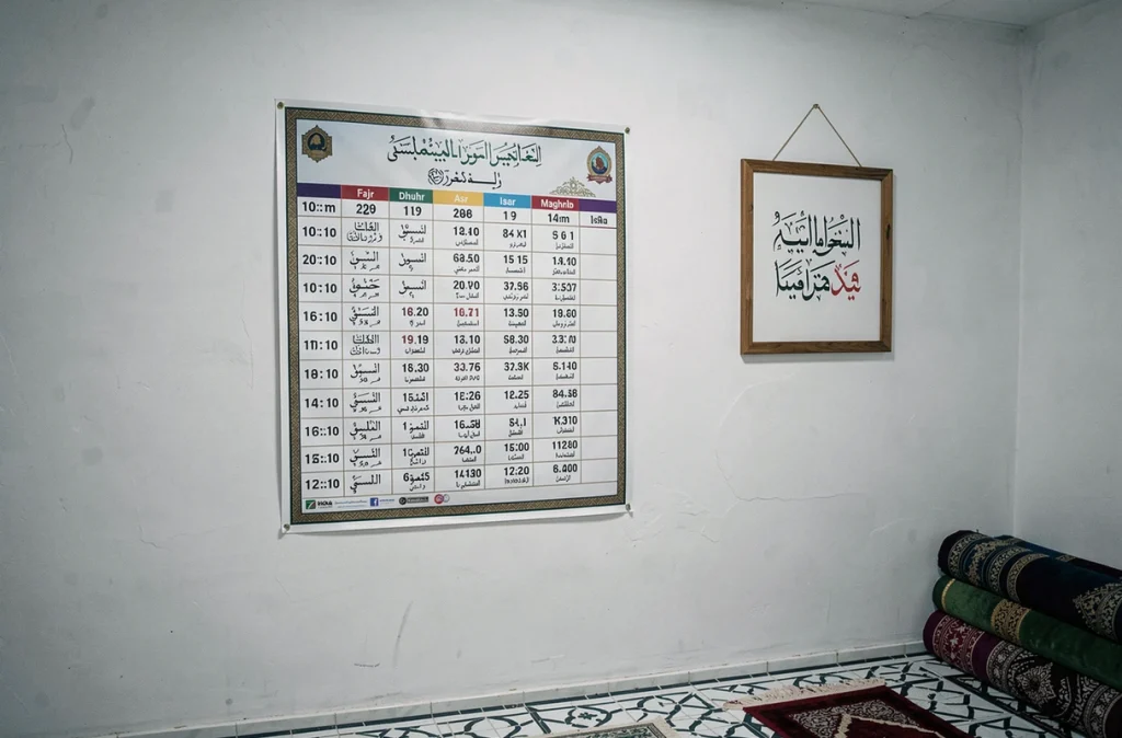 Affiche horaire de prière 2026 Mantes-la-Jolie affichée dans une salle de prière avec tapis enroulés et carrelage géométrique