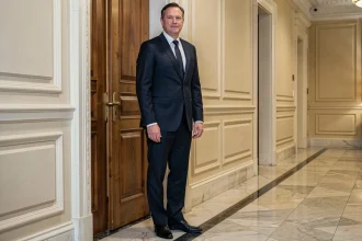 Homme en costume sombre debout dans un couloir institutionnel, illustrant la question de la taille d'Emmanuel Macron